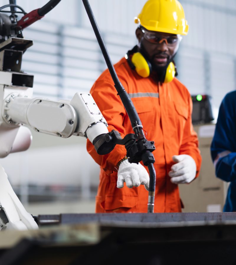 engineer cooperation male and female technician maintenance control relay robot arm system welding with tablet laptop to control quality operate process work heavy industry 4.0 manufacturing factory